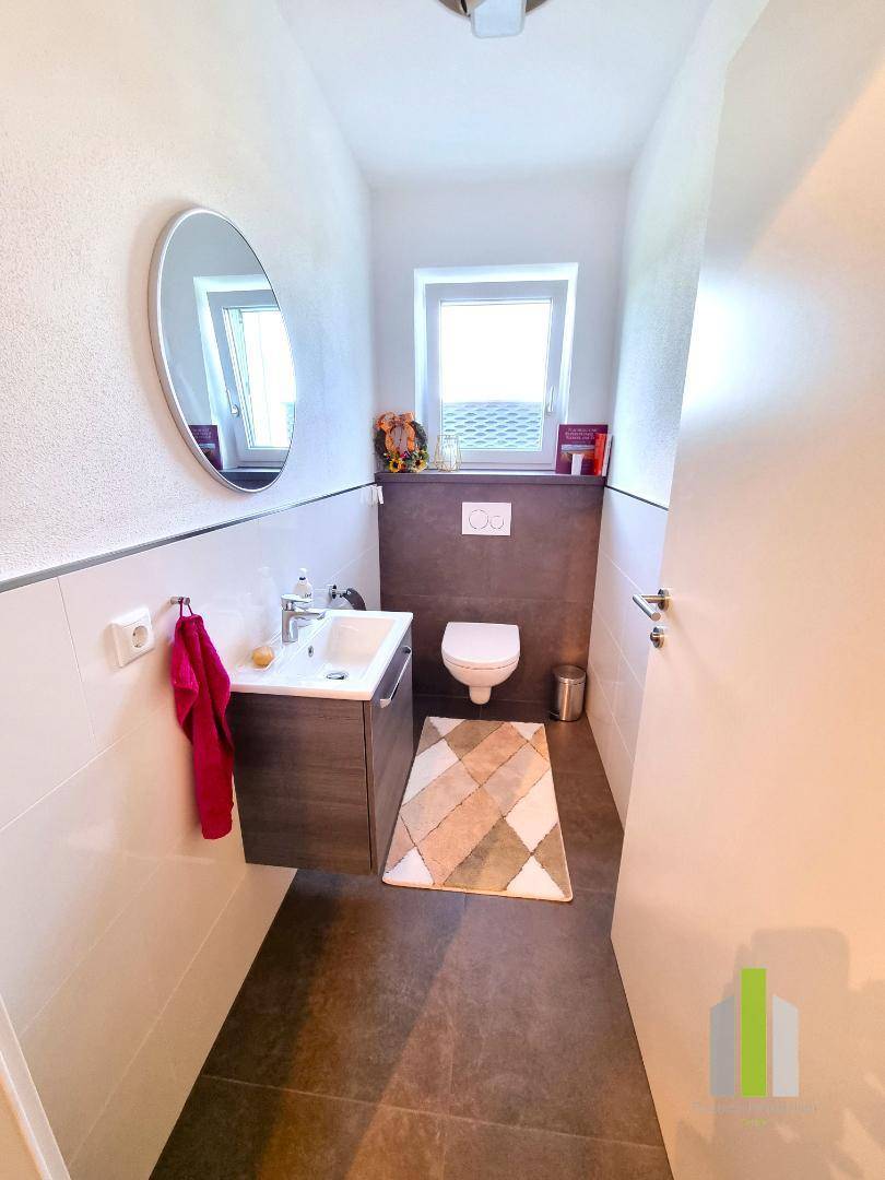 Modernes Gäste-WC mit wandhängendem WC, kleinem Waschbecken und Fenster für Tageslicht.