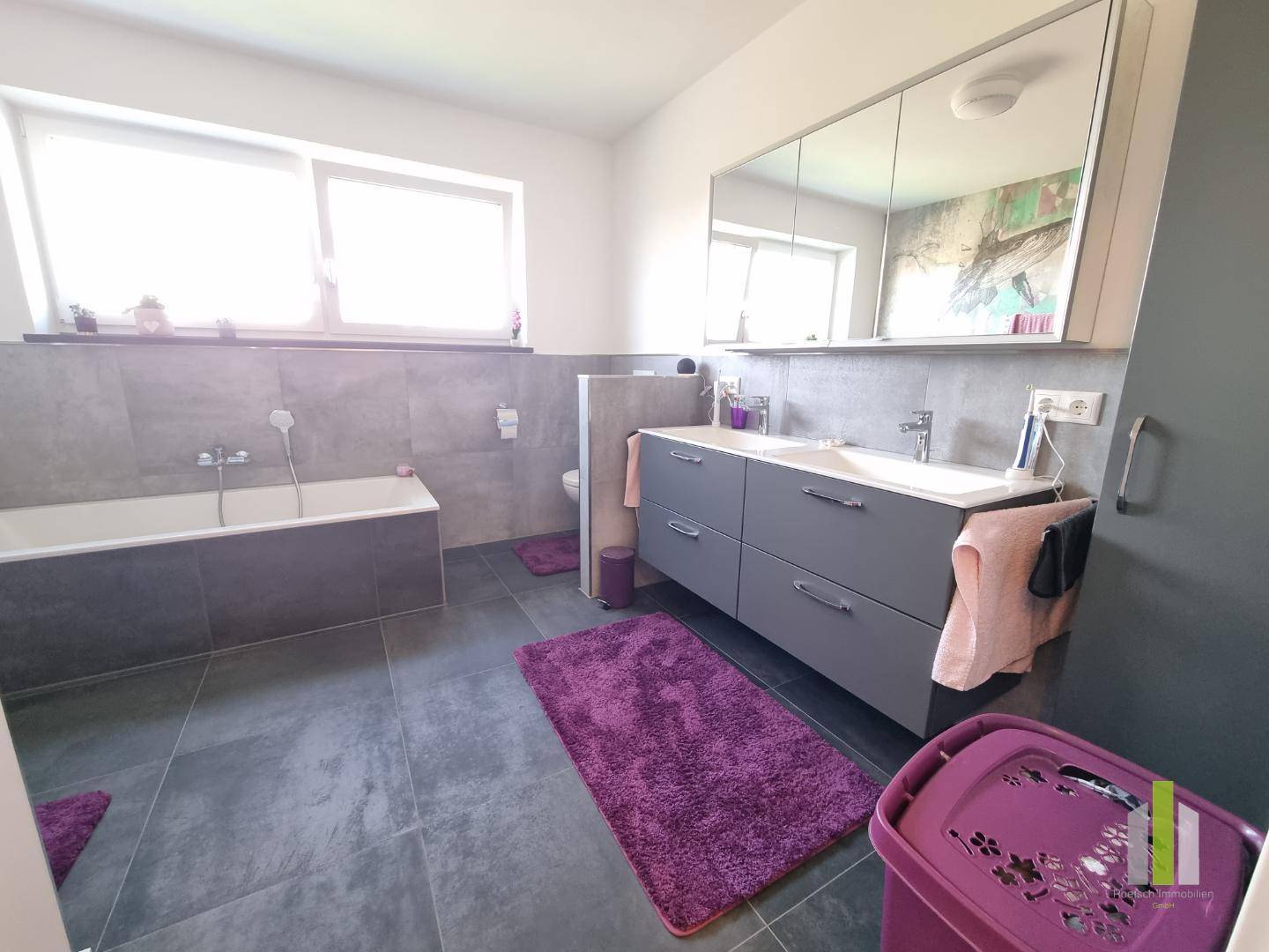 Modernes Badezimmer mit grauen Fliesen, Badewanne und Doppelwaschbecken mit Spiegelschrank.