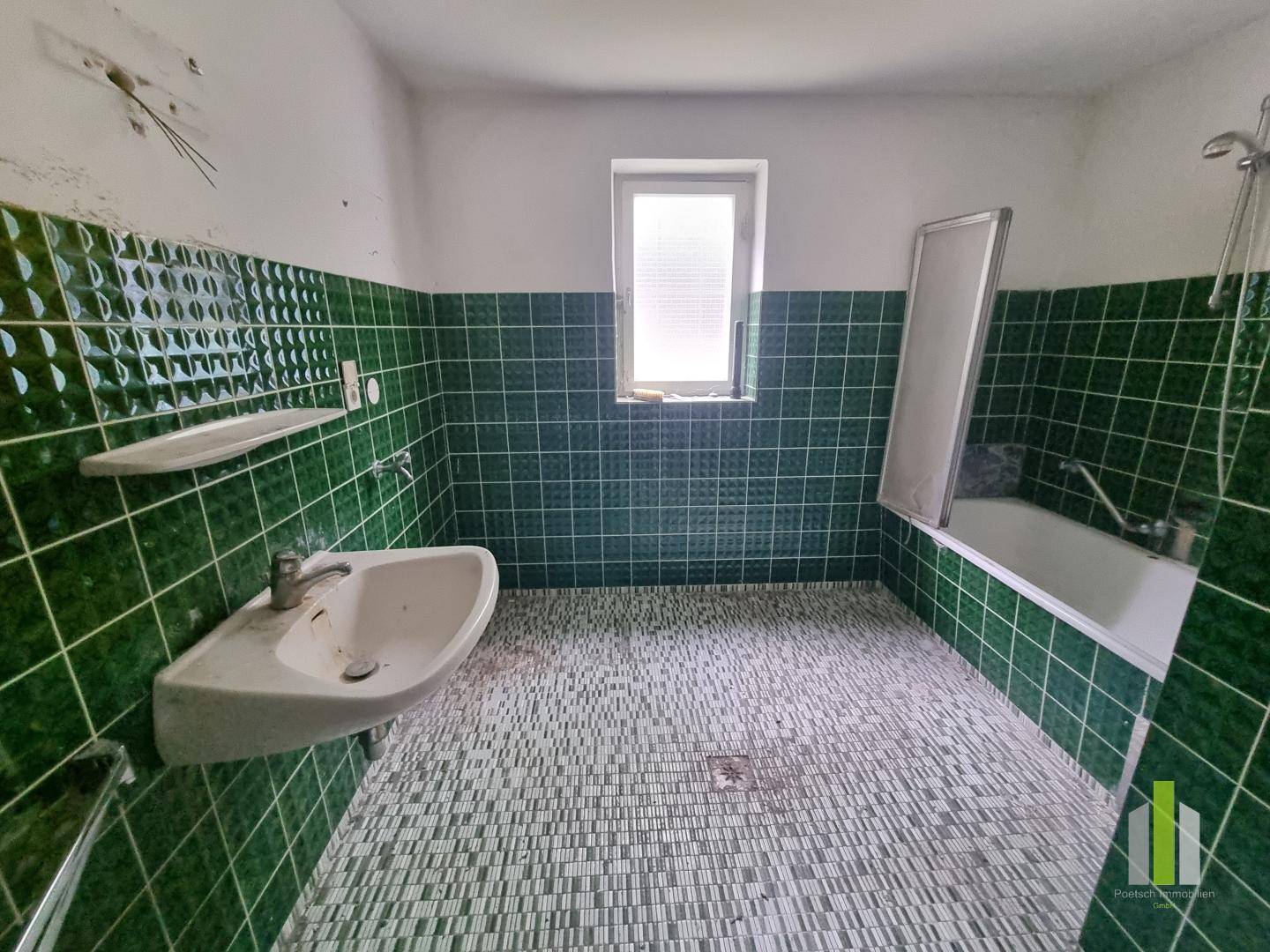 Badezimmer mit grünen Fliesen, Badewanne und Waschbecken, in originalem Zustand.