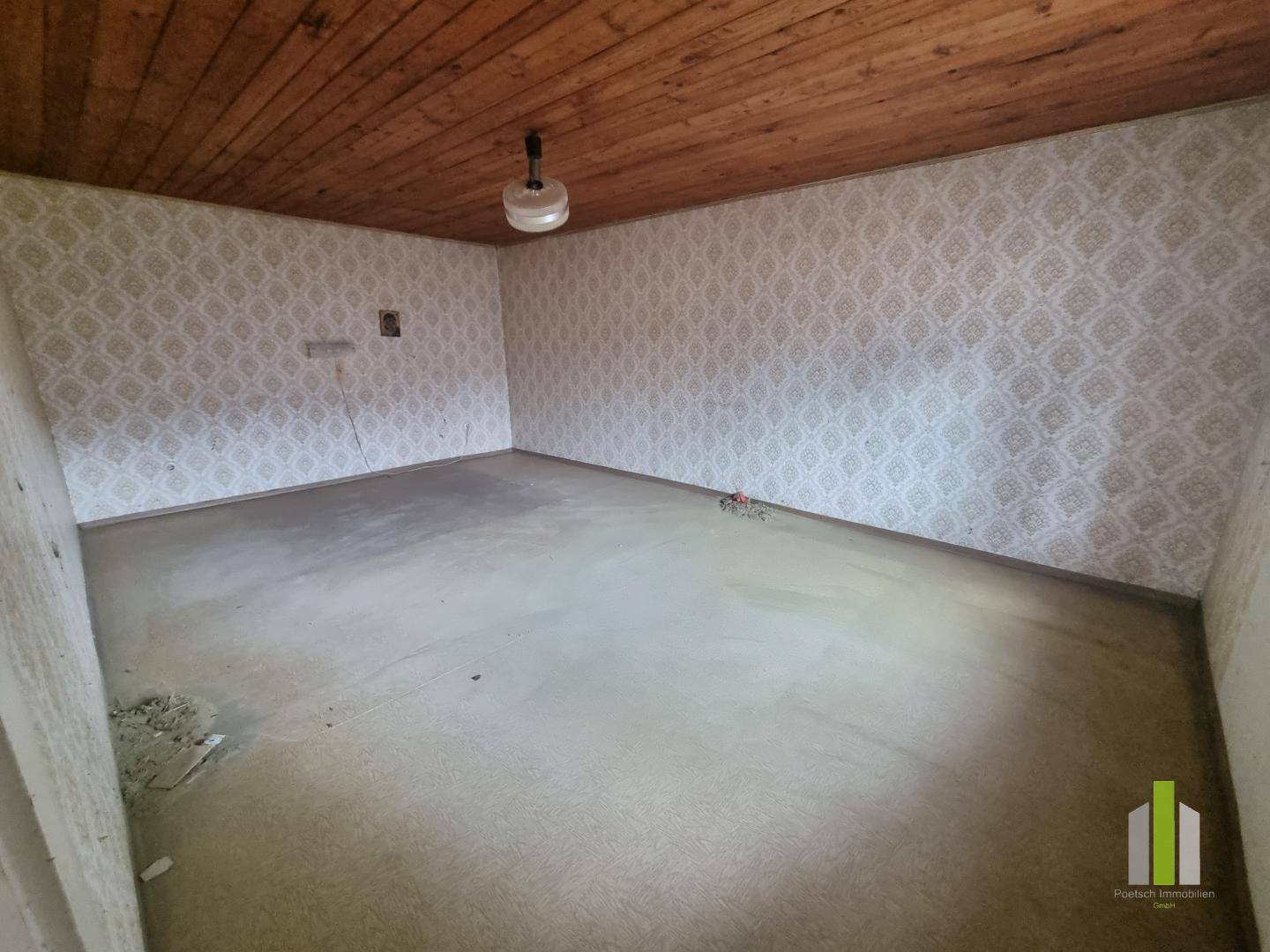 Zimmer mit gemusterter Tapete, Holzdecke und einfachem Bodenbelag, in originalem Zustand.