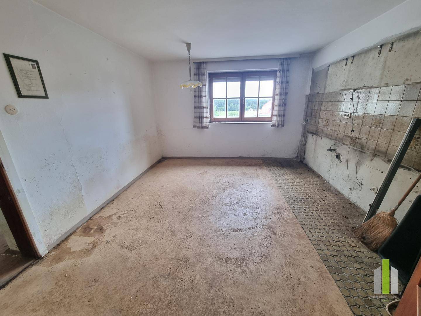 Renovierungsbedürftige Küche mit alten Fliesen an der Wand und Blick ins Grüne.