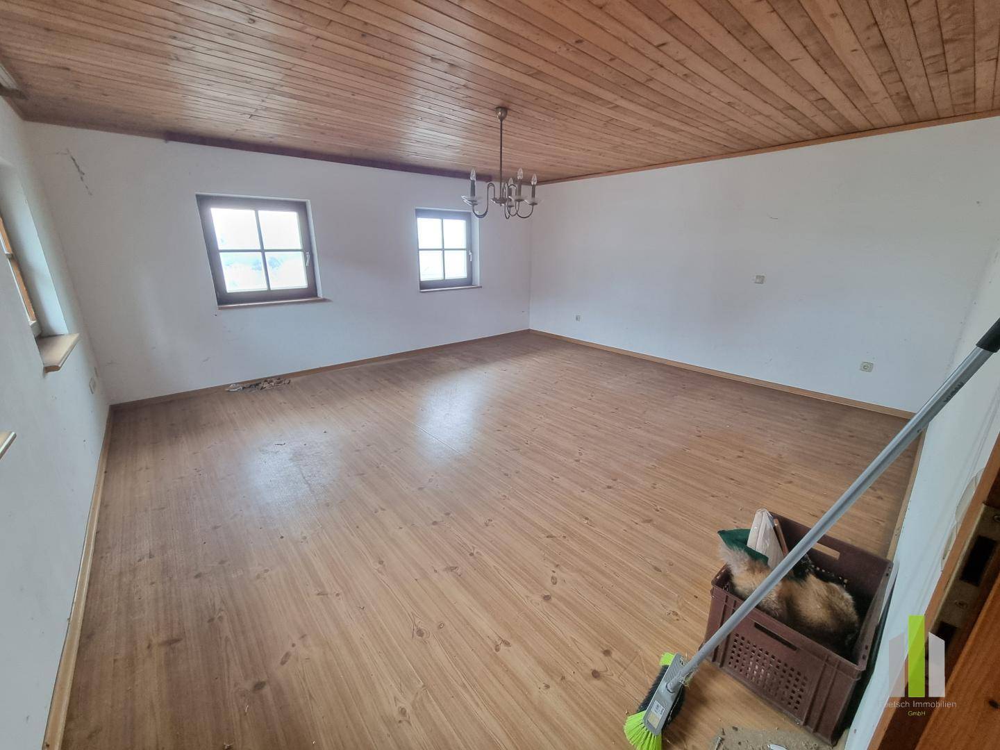 Großes Zimmer mit Holzdielenboden, Holzdecke und zwei Fenstern, bereit zur Renovierung.