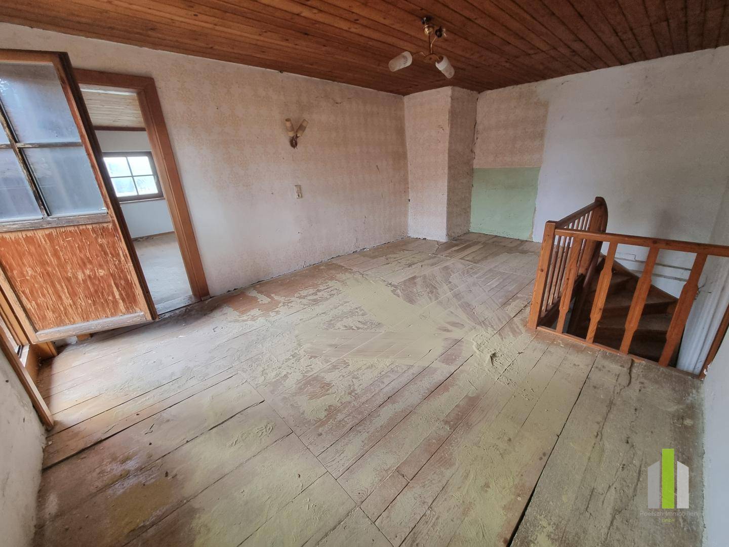 Obergeschosszimmer mit Holzdielenboden, Holzdecke und Zugang zu einem weiteren Raum.