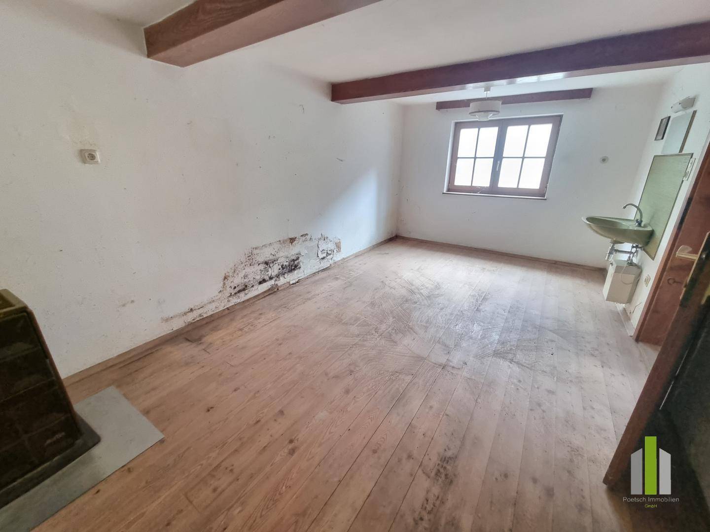 Helles Zimmer mit Holzdielenboden, Holzdecke und einem kleinen Waschbecken an der Wand.