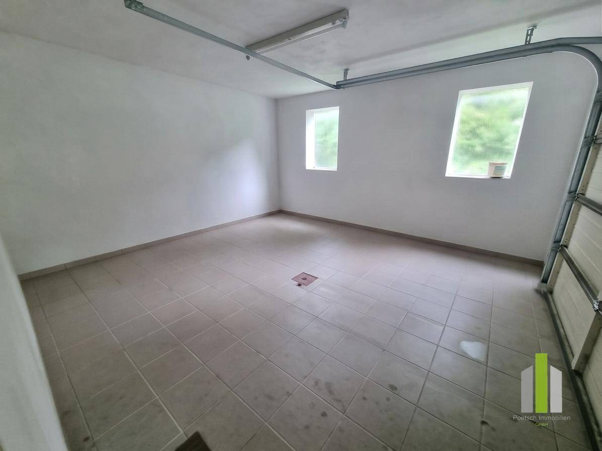 Geräumige Garage mit Fliesenboden und zwei Fenstern, bietet Platz für ein Fahrzeug.