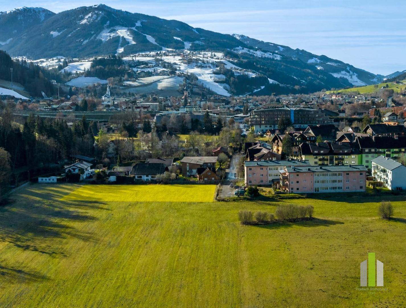 Weitläufige Luftaufnahme eines Baugrundstücks mit Blick auf die Stadt und schneebedeckte Berge.