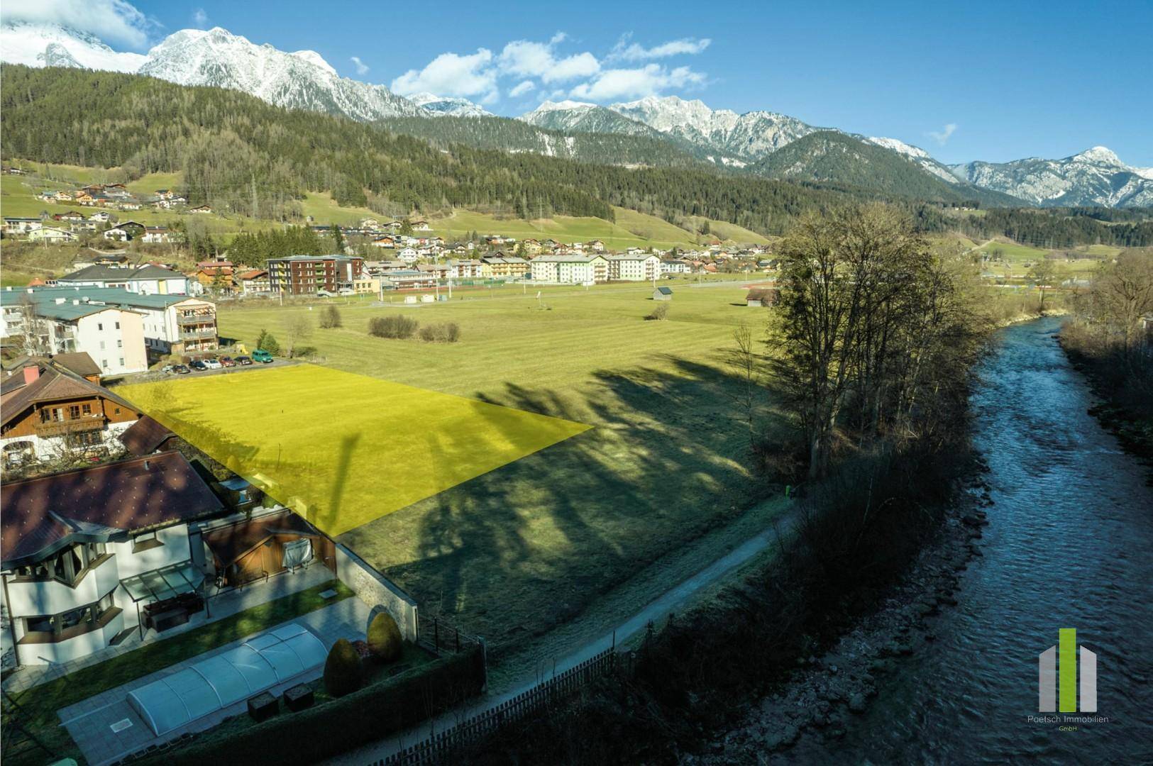Luftaufnahme eines grünen Grundstücks am Flussufer mit gelb markierter Fläche und Bergblick.