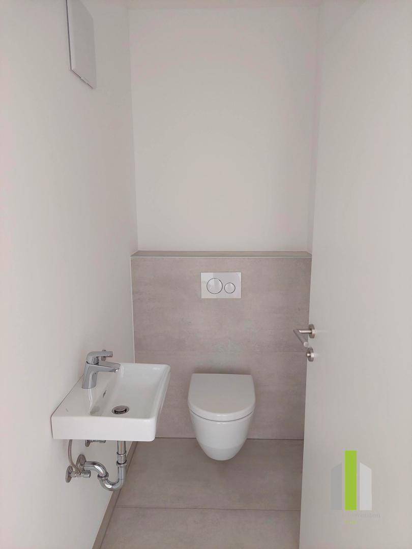 Kompaktes Gäste-WC mit wandhängender Toilette, kleinem Waschbecken und modernen Fliesen.