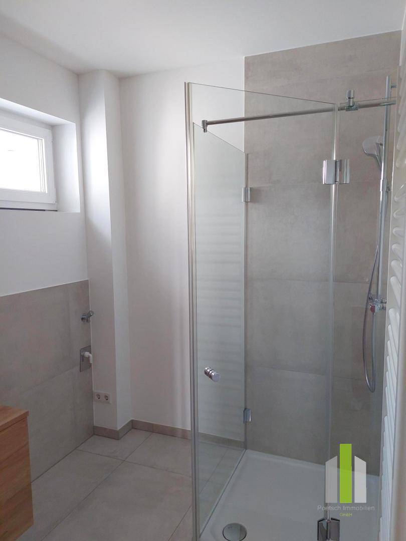 Helles Badezimmer mit moderner Glasdusche, hellen Fliesen und kleinem Fenster für Tageslicht.