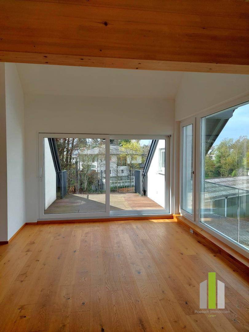 Lichtdurchfluteter Wohnbereich mit Holzboden, großen Schiebetüren zur Terrasse und sichtbarem Holzbalken.