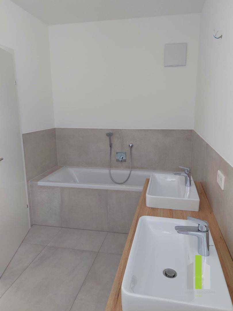Modernes Badezimmer mit eingebauter Badewanne, zwei Aufsatzwaschbecken und hellen Fliesen.
