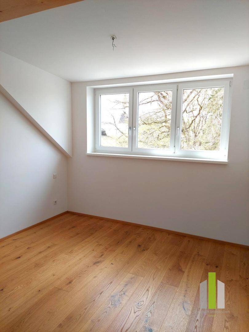 Helles Schlafzimmer mit Holzboden, weiß gestrichenen Wänden und großem Fenster unter Dachschräge.