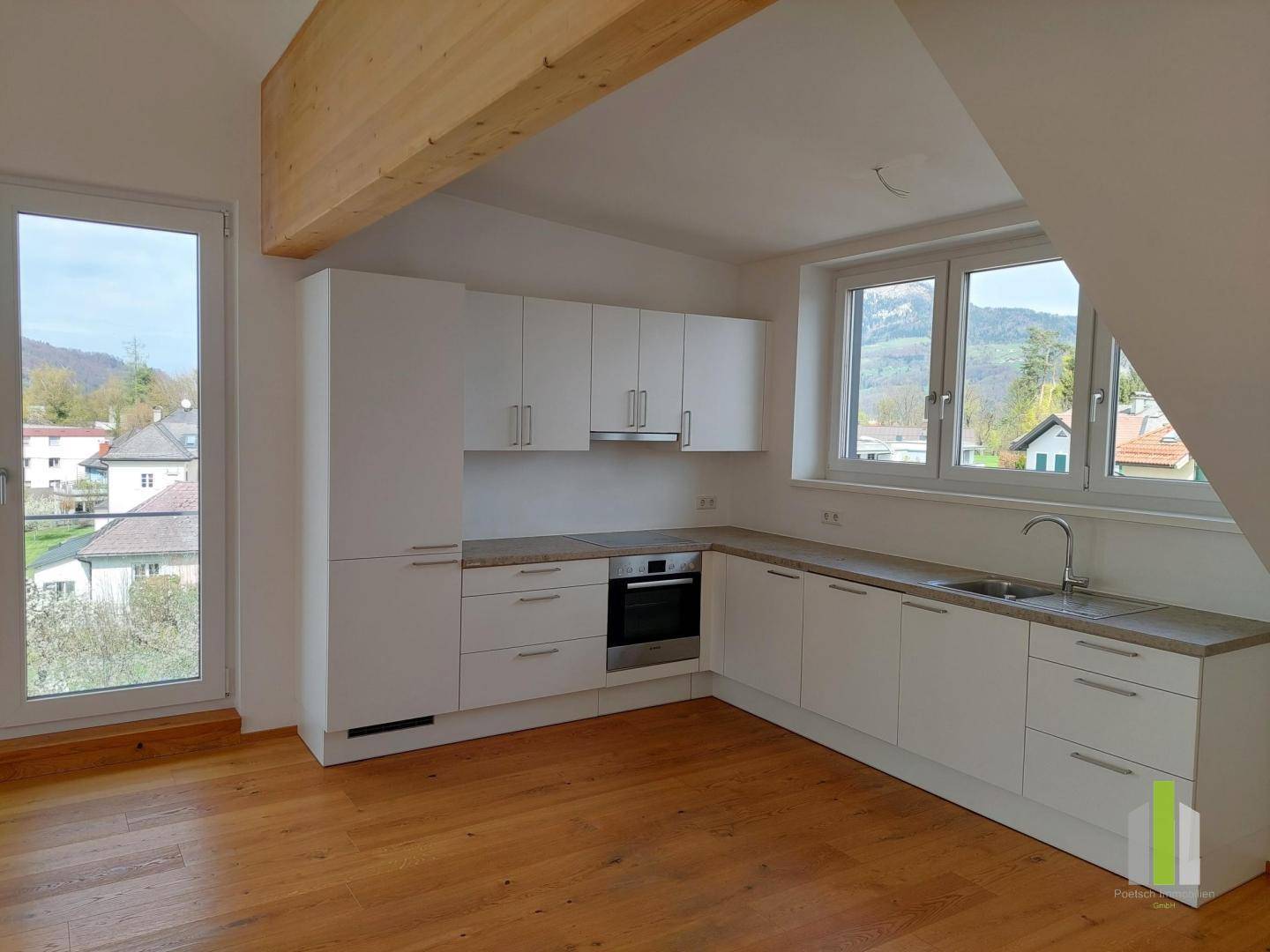 Helle Küche mit weißen Schränken, Holzboden und Bergblick, offen gestaltet mit sichtbarem Holzbalken.