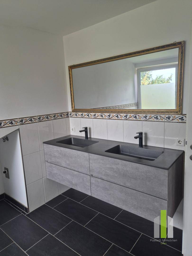 Modernes Badezimmer mit Doppelwaschbecken, dunklen Fliesen und einem großen Spiegel.
