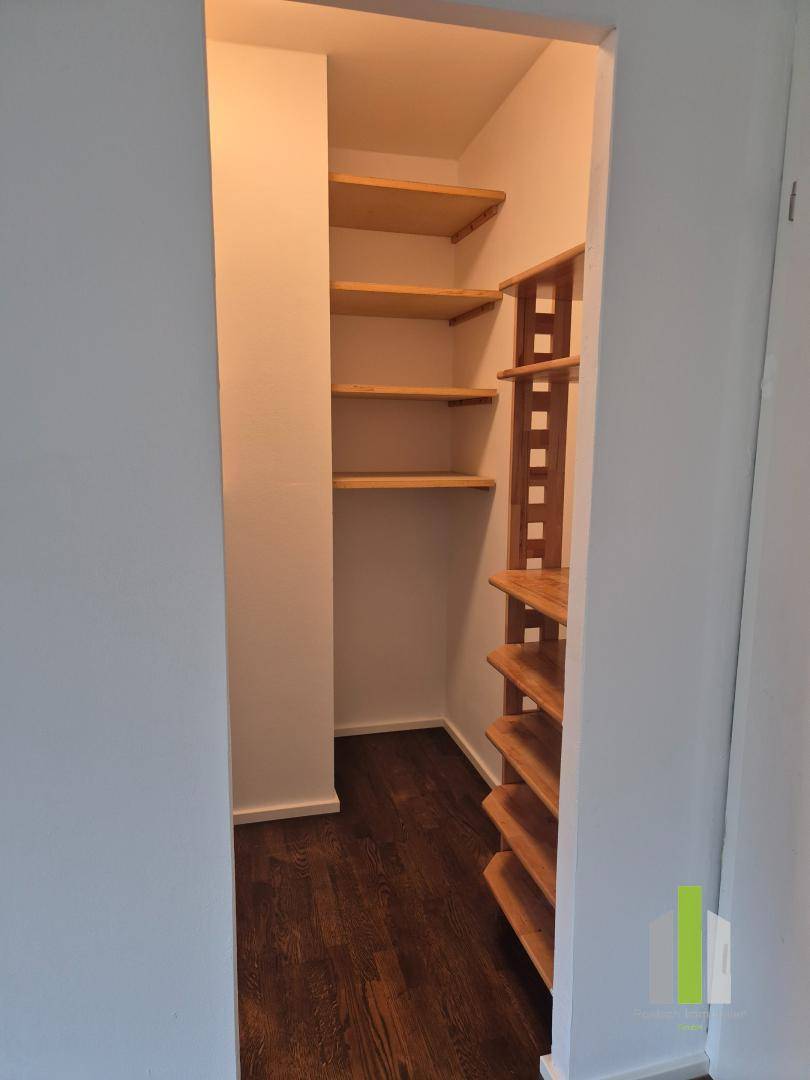 Praktischer Abstellraum mit Holzregalen und dunklem Holzboden, ideal für Vorräte oder Lagerung.