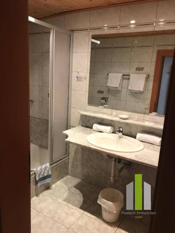 Badezimmer mit Duschkabine, Waschbecken und hellen Fliesen.