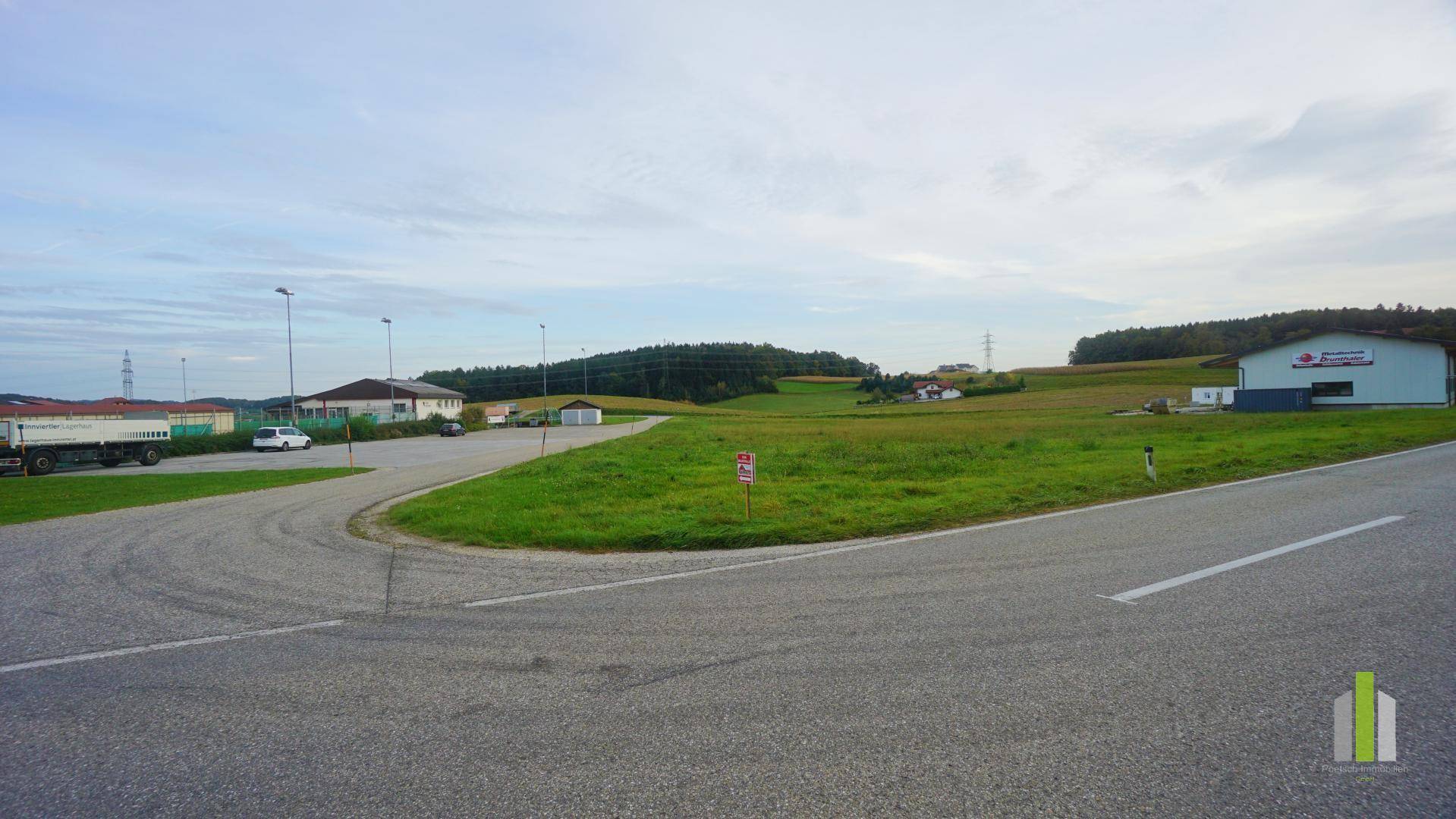 Weitläufige Landschaft mit Straßen, grünen Wiesen und vereinzelten Gebäuden am Horizont unter bewölktem Himmel.