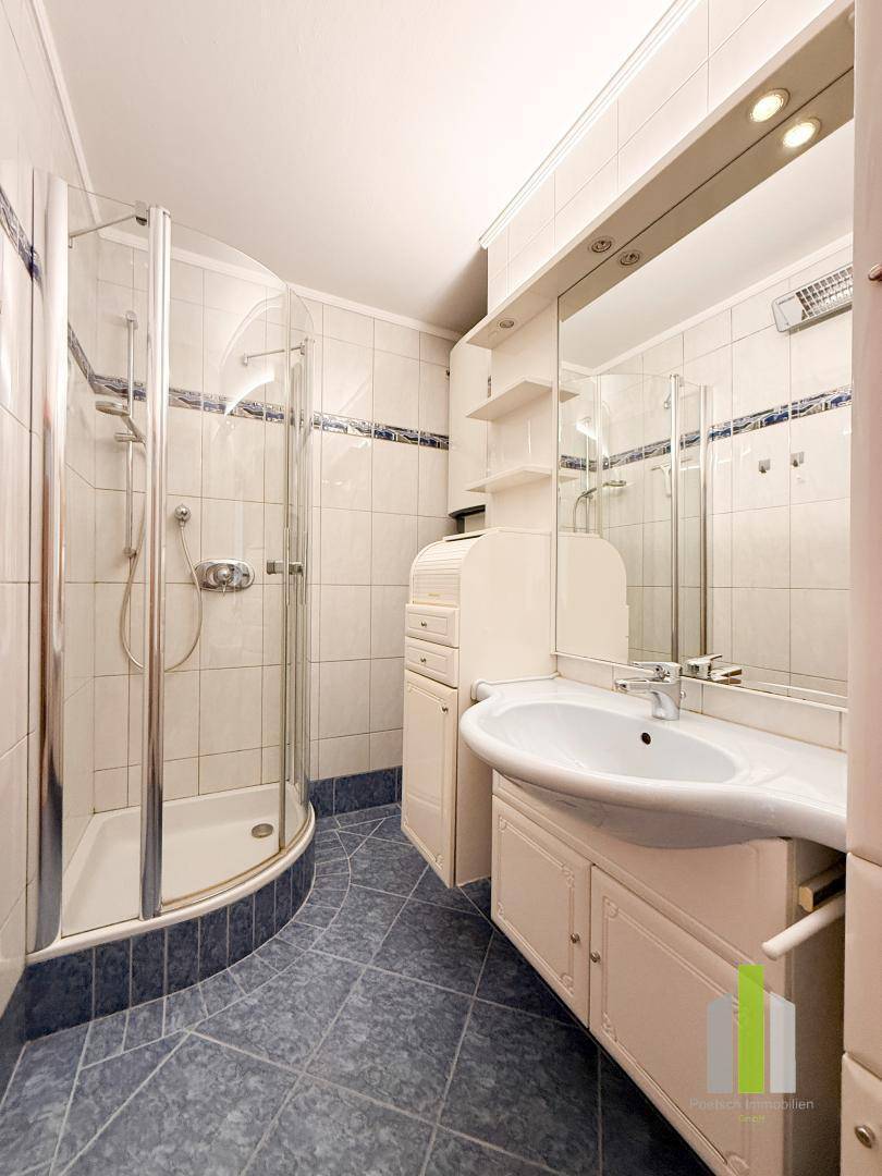 Badezimmer mit Duschkabine, Waschbecken und blauen Bodenfliesen in gutem Zustand.