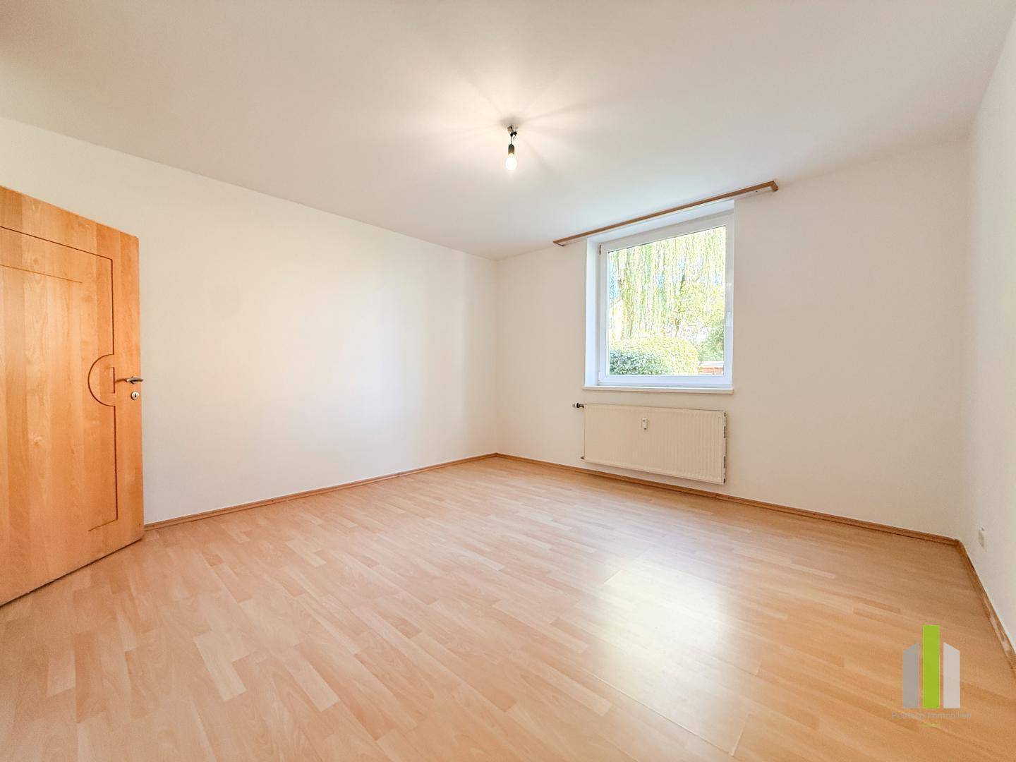 Ruhiges Schlafzimmer mit Parkettboden und einem Fenster mit Blick ins Grüne.
