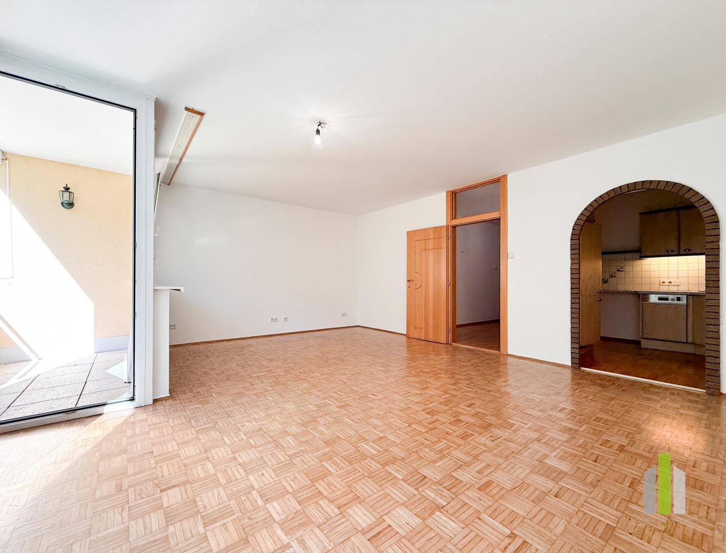 Geräumiges Wohnzimmer mit Parkettboden, Balkonzugang und einem Durchgang zur Küche.