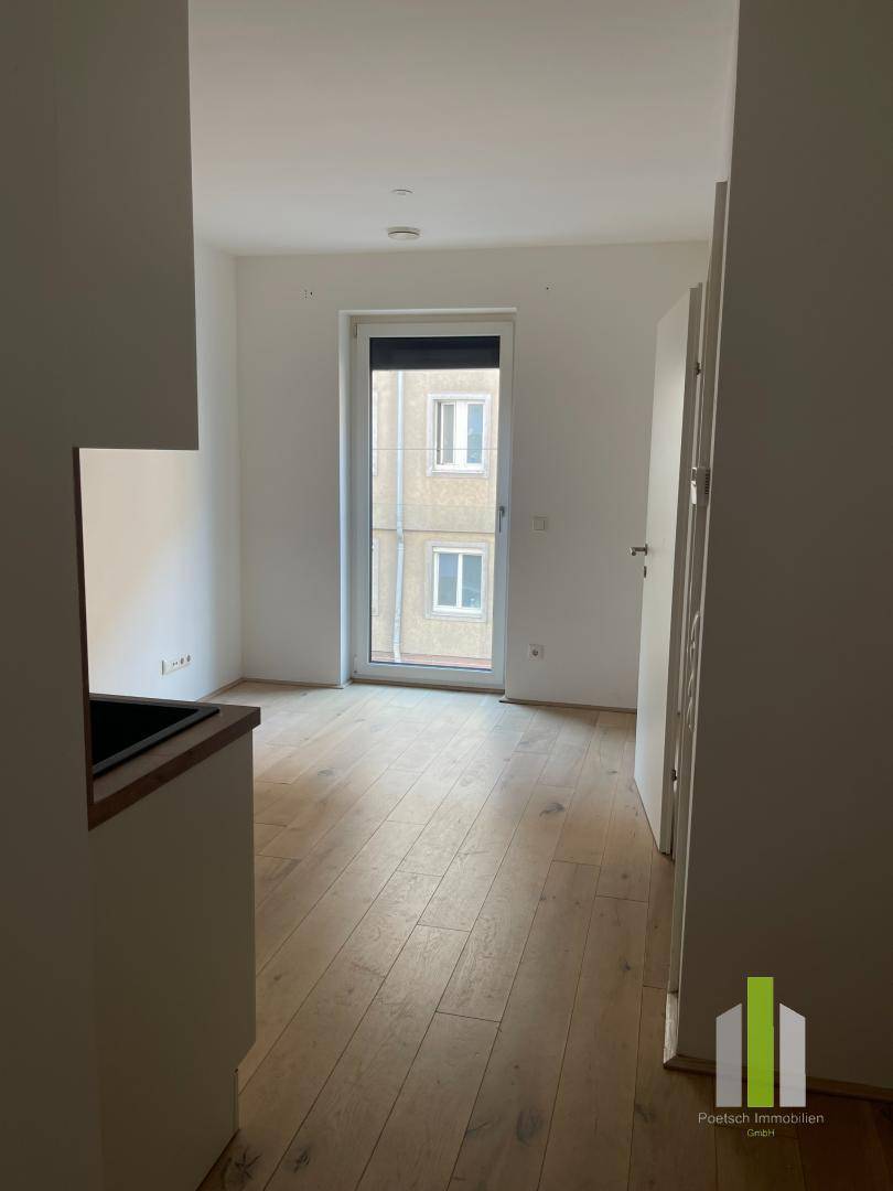 Heller Wohnraum mit Holzboden und einer Tür, die zu einem kleinen Balkon oder einer französischen Tür führt.