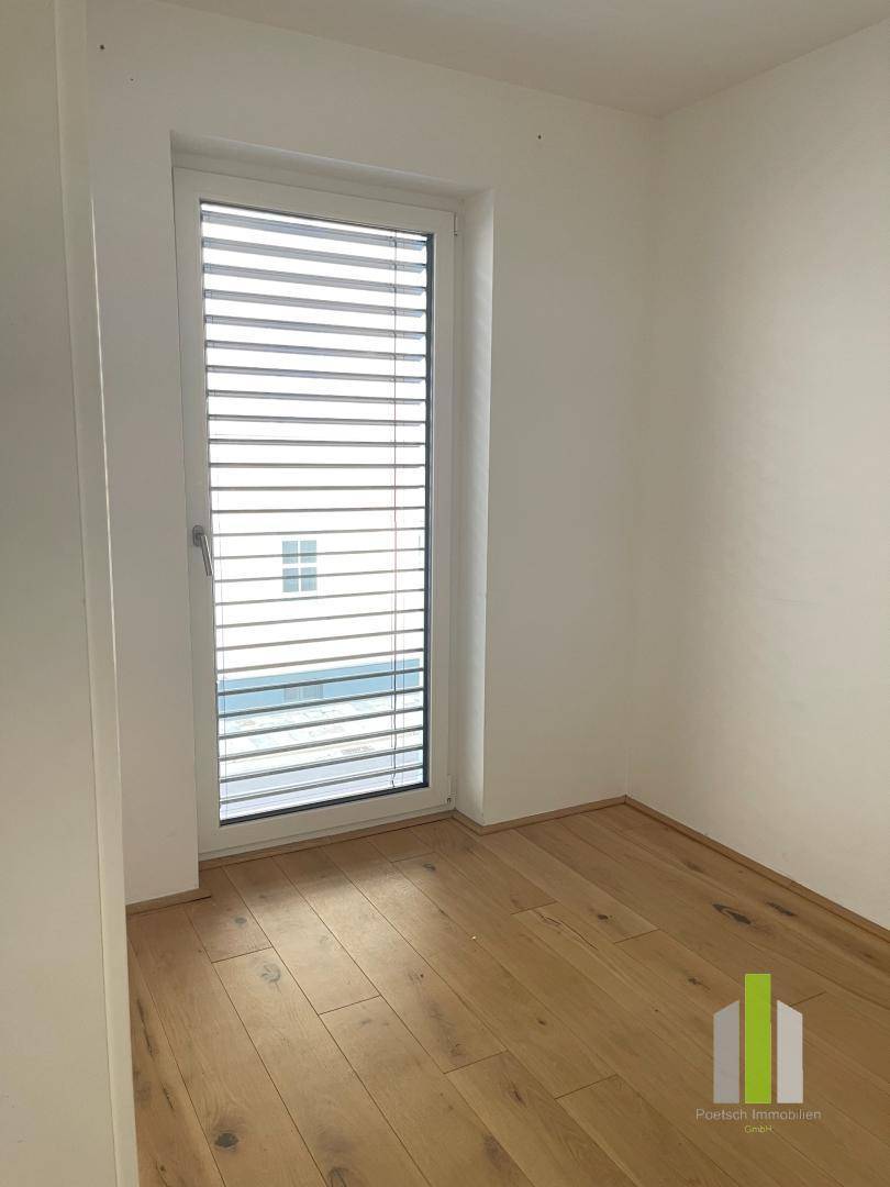 Helles Zimmer mit Holzboden und einem Fenster mit Jalousien, ideal als Schlaf- oder Arbeitszimmer nutzbar.