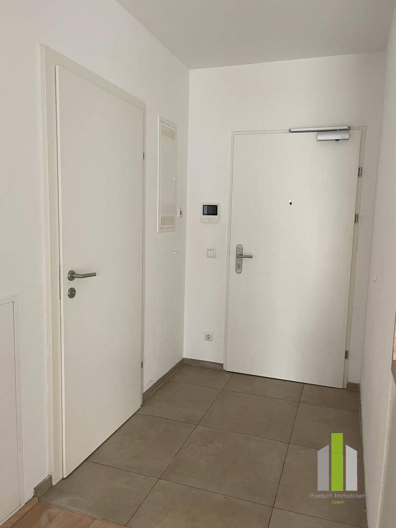 Heller Eingangsbereich mit Fliesenboden und mehreren weißen Türen, die zu den verschiedenen Zimmern führen.