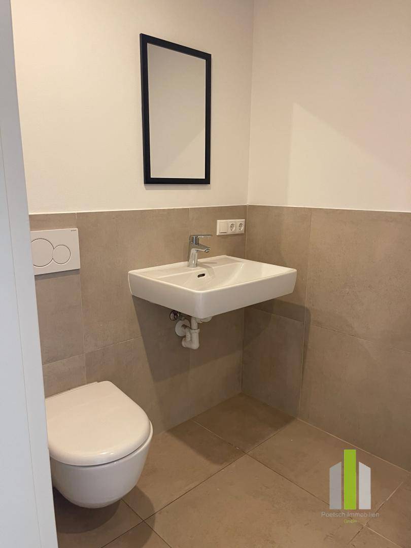 Modernes Gäste-WC mit wandhängender Toilette, kleinem Waschbecken und hellen Fliesen an Wänden und Boden.