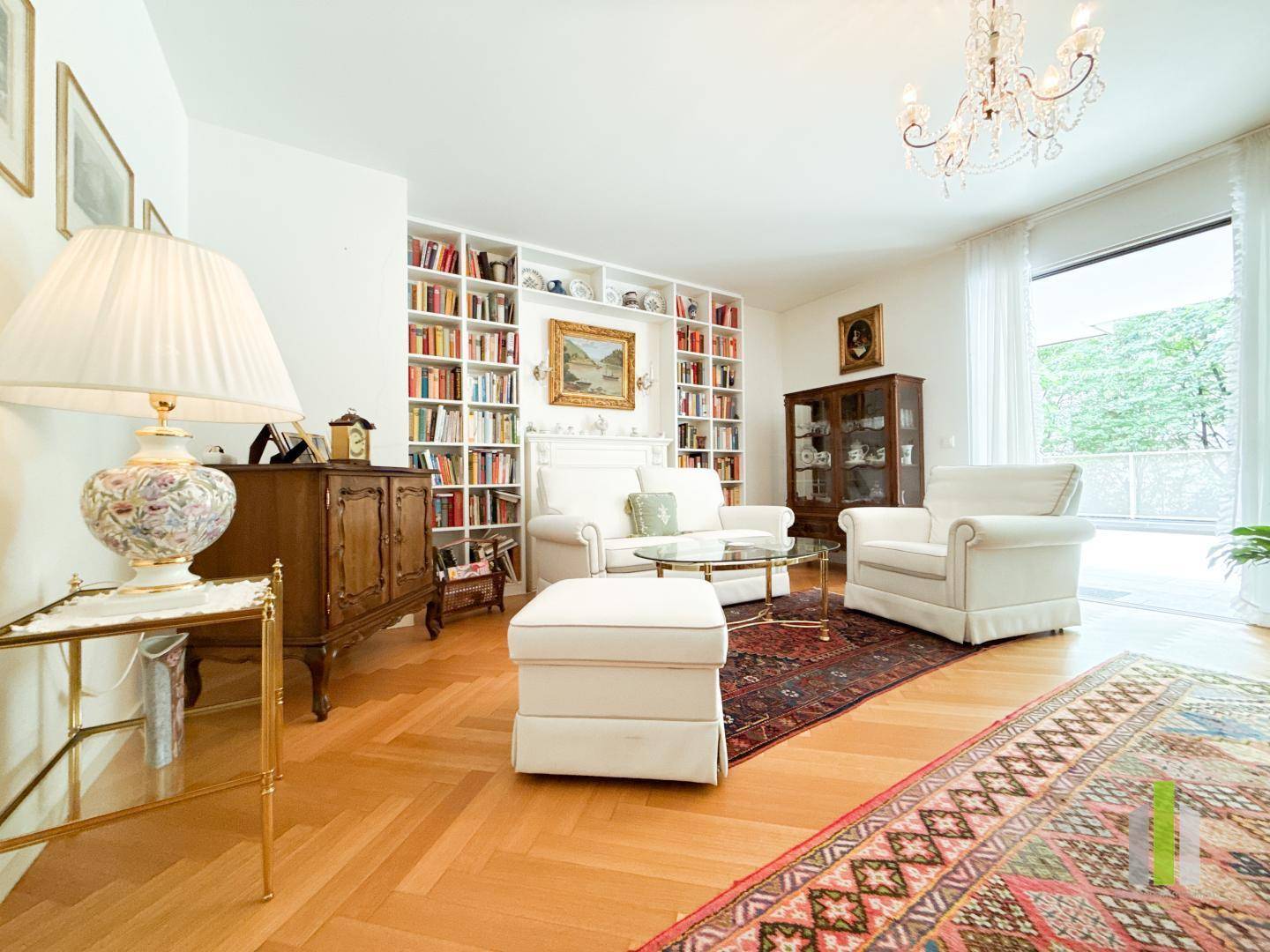 Elegantes Wohnzimmer mit Fischgrätparkett, Bücherregal und klassischem Kronleuchter.