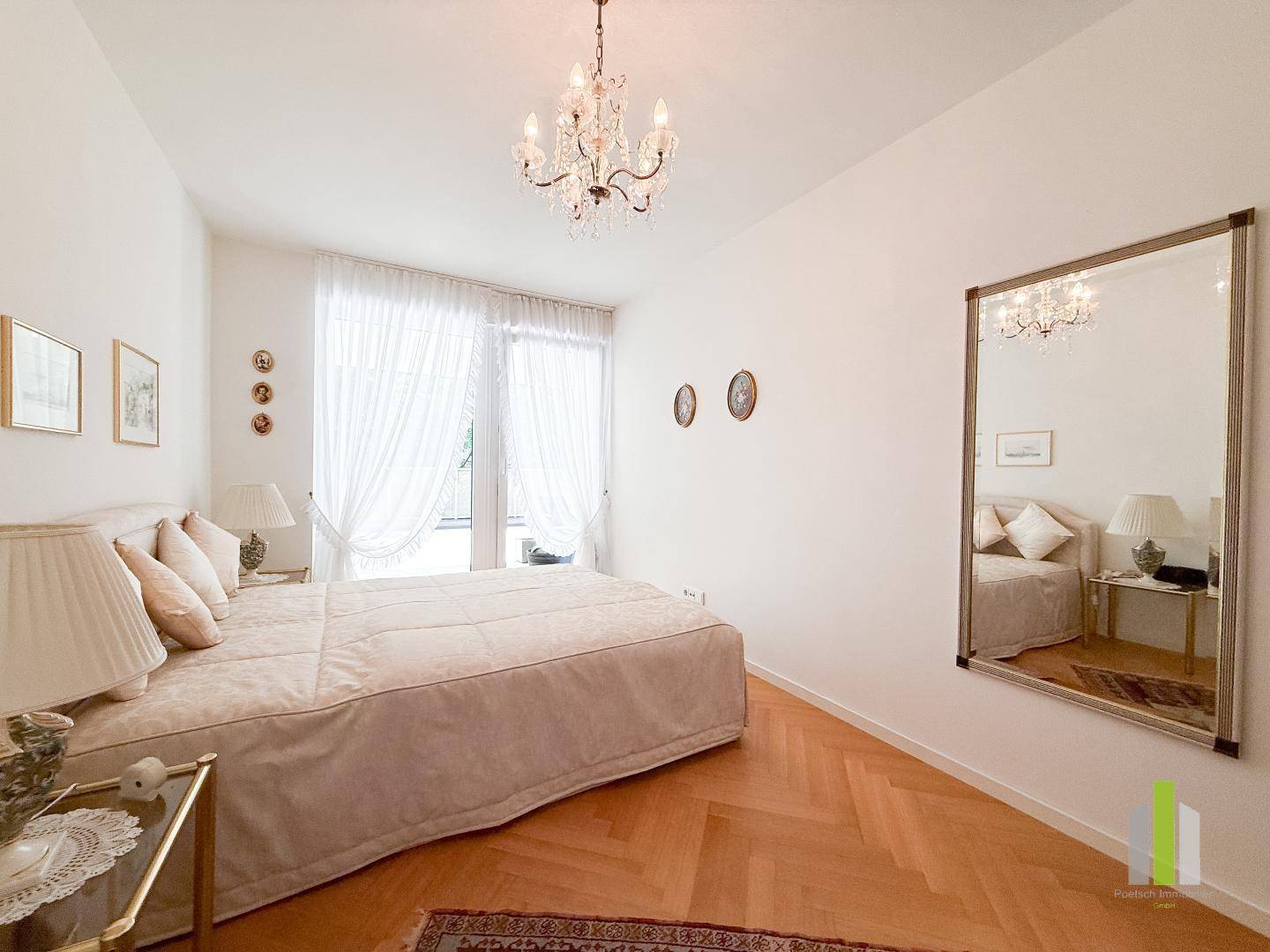 Helles Schlafzimmer mit Fischgrätparkett, großem Spiegel und elegantem Kronleuchter.