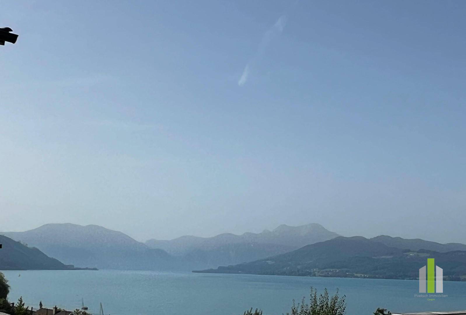 Weitläufiger Blick über einen ruhigen See und die umliegende Berglandschaft unter einem klaren Himmel.