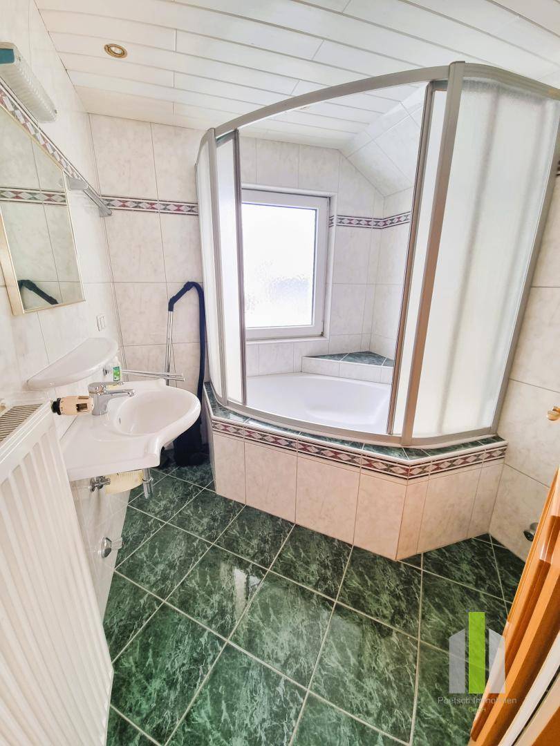 Badezimmer mit Eckbadewanne, Duschkabine und grün gemusterten Fliesen.