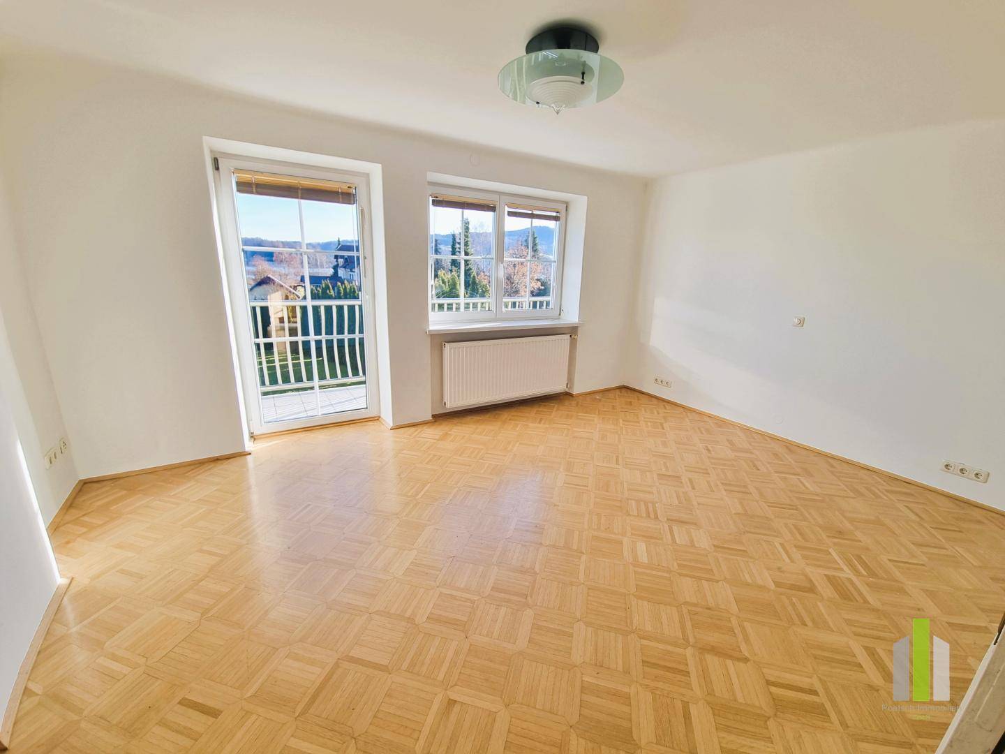 Helles Zimmer mit Parkettboden und Zugang zu einem französischen Balkon.
