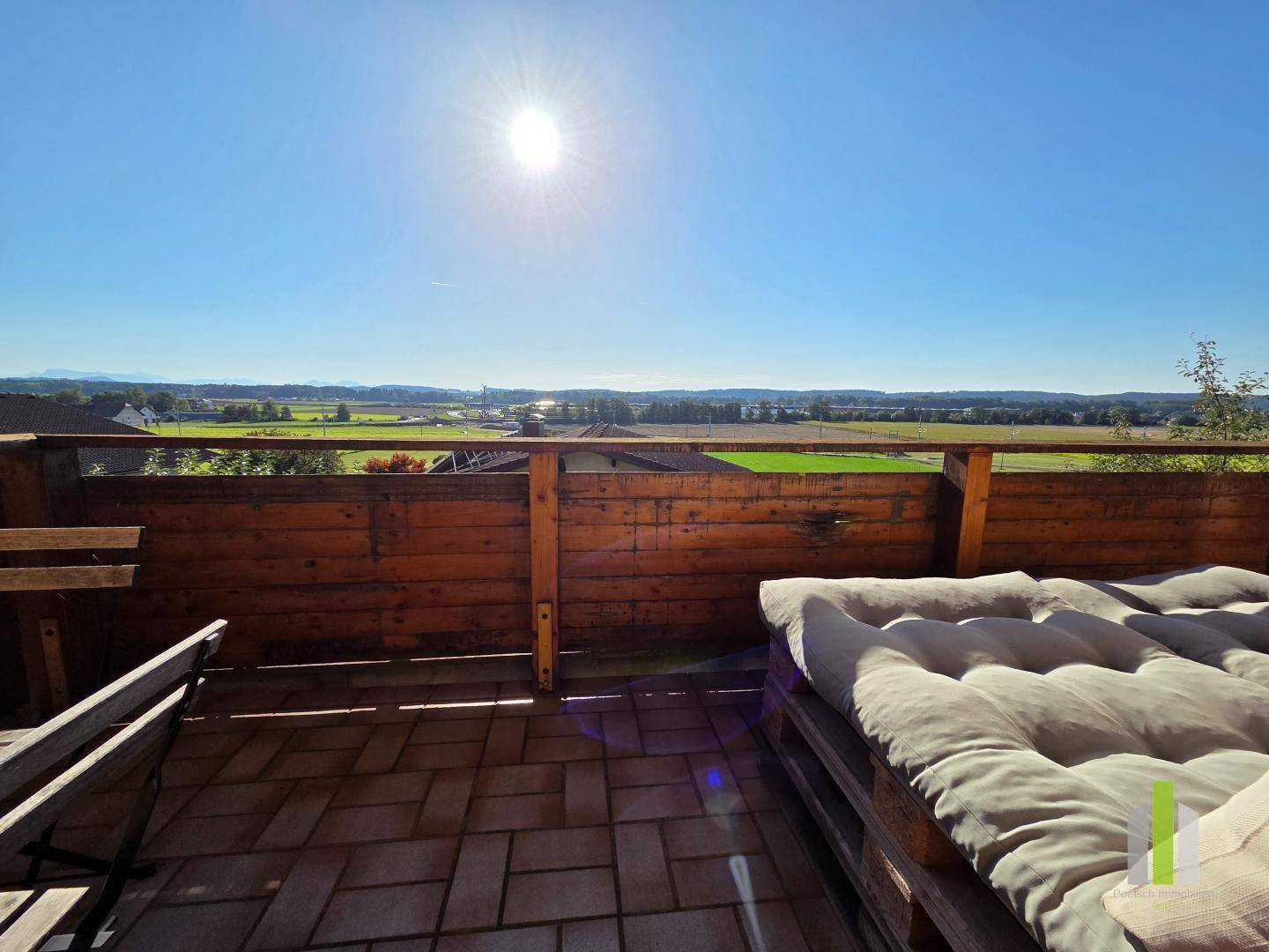 Sonniger Balkon mit Sitzgelegenheiten und weitem Blick über die grüne Landschaft.