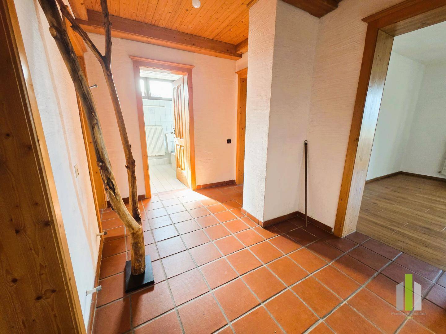 Geräumiger Flur mit Terrakottafliesen, Holztüren und natürlichem Lichteinfall durch die Fenster.