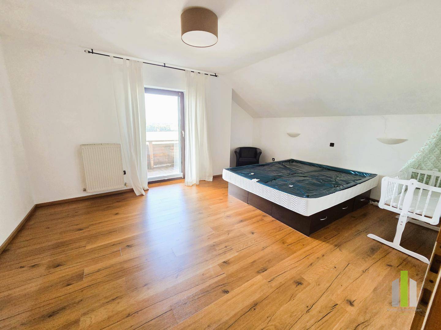 Helles Schlafzimmer mit Holzboden, Dachschräge und direktem Zugang zu einem Balkon.