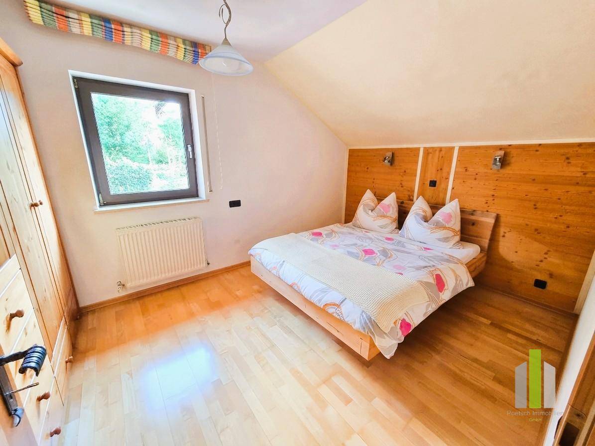 Schlafzimmer mit Holzboden, Holzwandverkleidung und Fenster mit Blick ins Grüne.