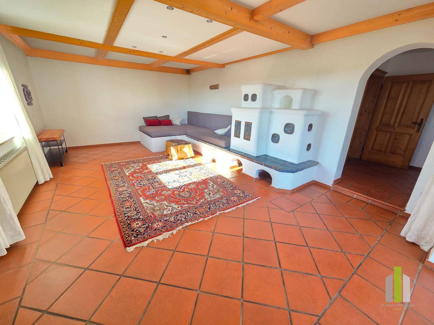 Gemütliches Wohnzimmer mit Terrakottafliesen, Holzbalkendecke und traditionellem Kachelofen.