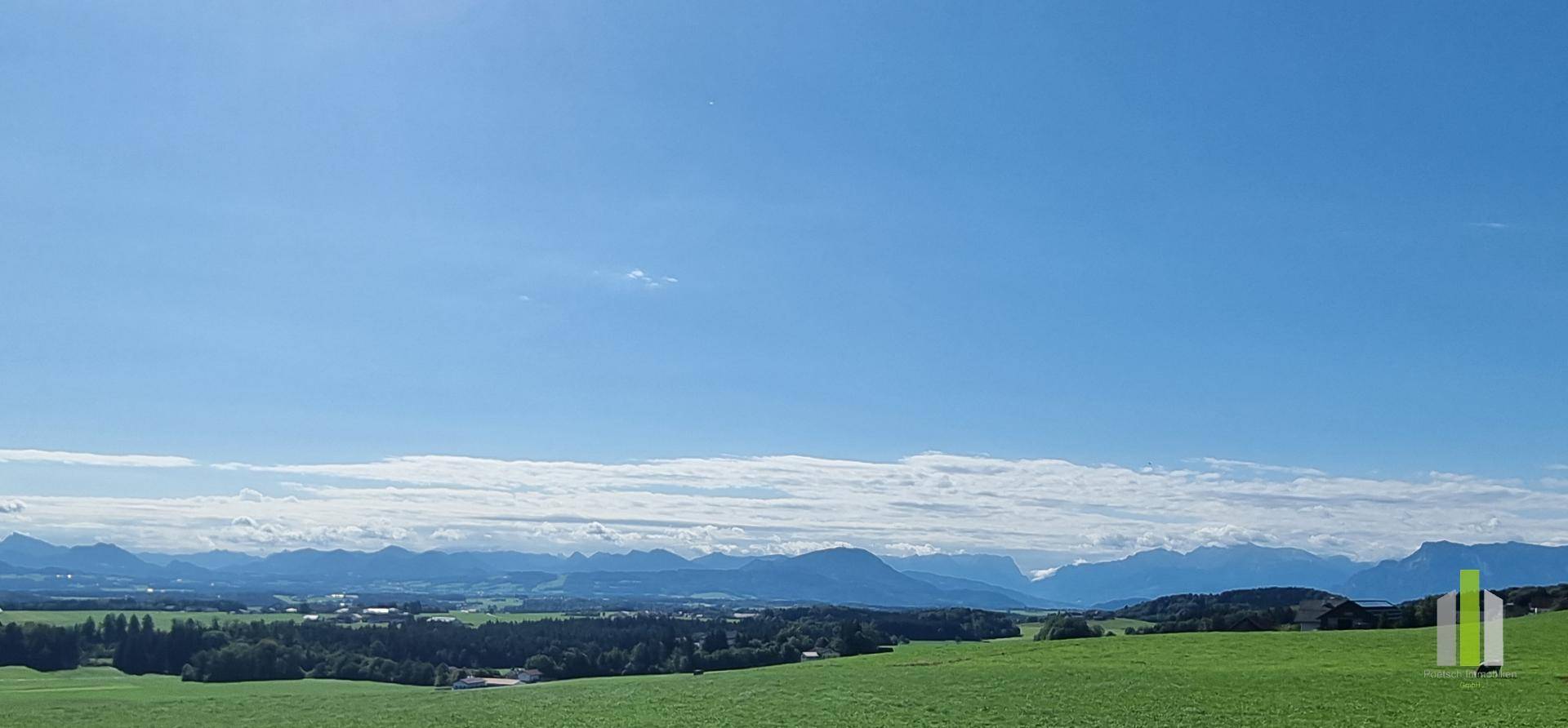 Weitläufiger Panoramablick über grüne Felder und eine beeindruckende Bergkette am Horizont.