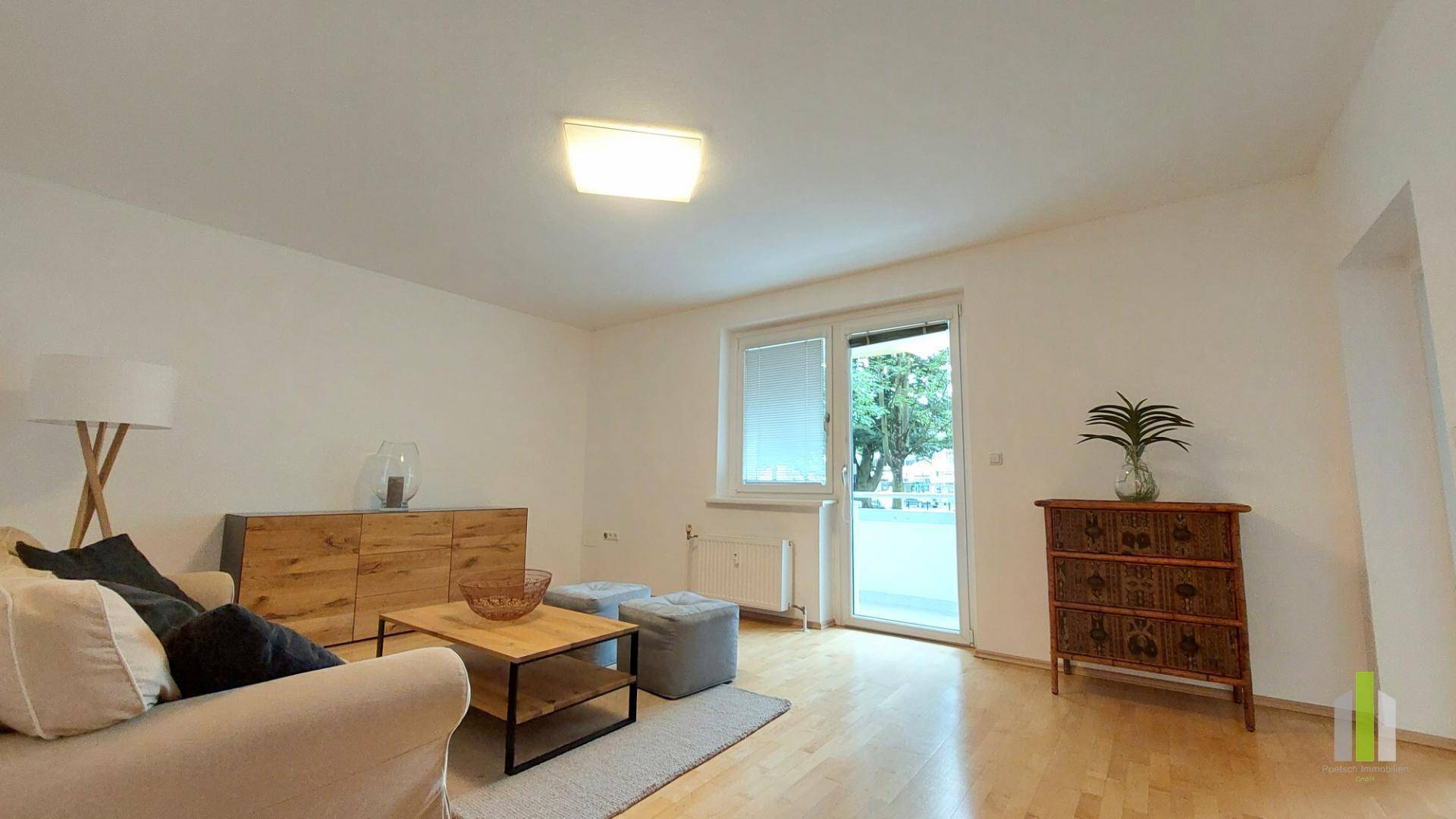Helles Wohnzimmer mit beigem Sofa, Holzboden und Zugang zu einem Außenbereich.