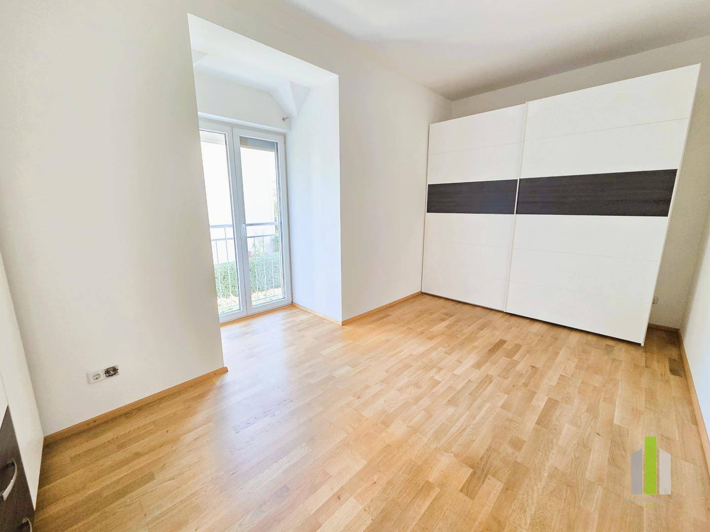 Schlafzimmer mit Holzboden, großem Schrank und Zugang zu einem französischen Balkon.