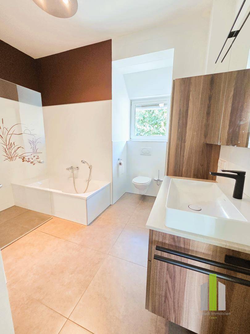 Modernes Badezimmer mit Badewanne, Waschtisch und Fenster für ausreichend Tageslicht.