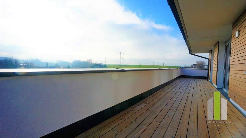 Lange Dachterrasse mit Holzboden und Blick auf die grüne Umgebung und Strommasten in der Ferne.