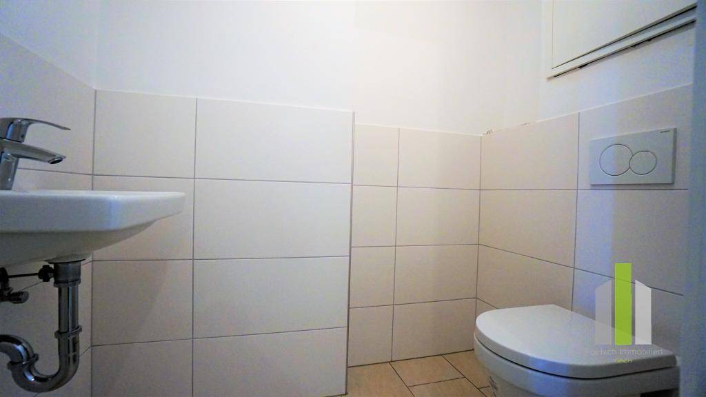 Separates Gäste-WC mit Waschbecken und wandhängender Toilette, ausgestattet mit hellen Fliesen.