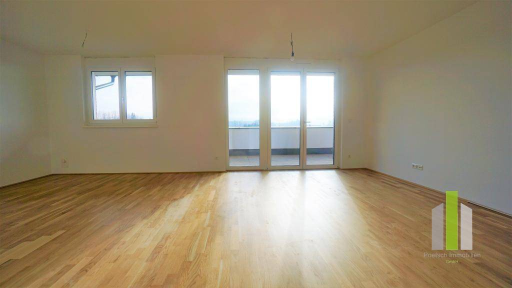 Helles, leeres Wohnzimmer mit Holzboden, weißen Wänden und Zugang zu einem Balkon oder einer Terrasse.