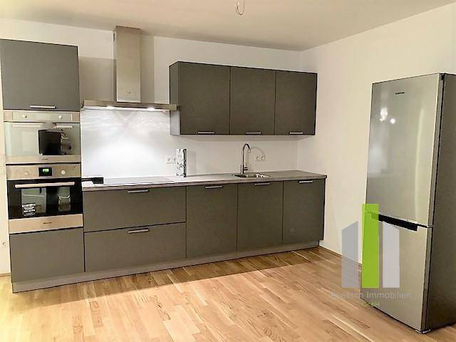 Moderne Küche mit grauen Schränken, integrierten Geräten und einem Kühlschrank auf hellem Holzboden.