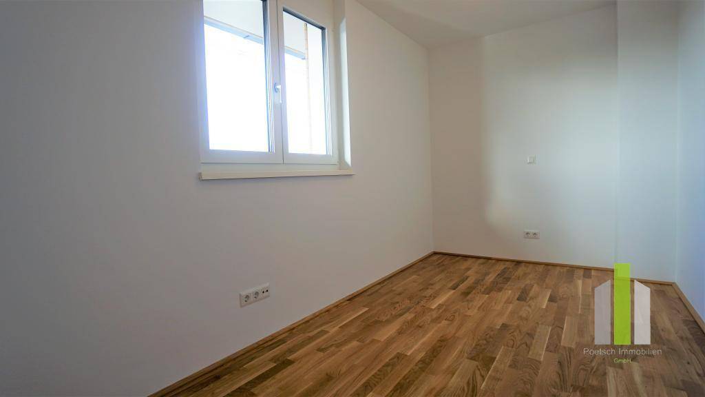 Helles Schlafzimmer mit Holzboden und einem großen Fenster, das viel Tageslicht hereinlässt.