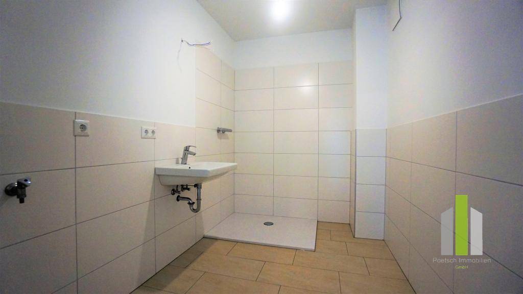 Modernes Badezimmer mit hellen Fliesen, einem Waschbecken und einer ebenerdigen Dusche.