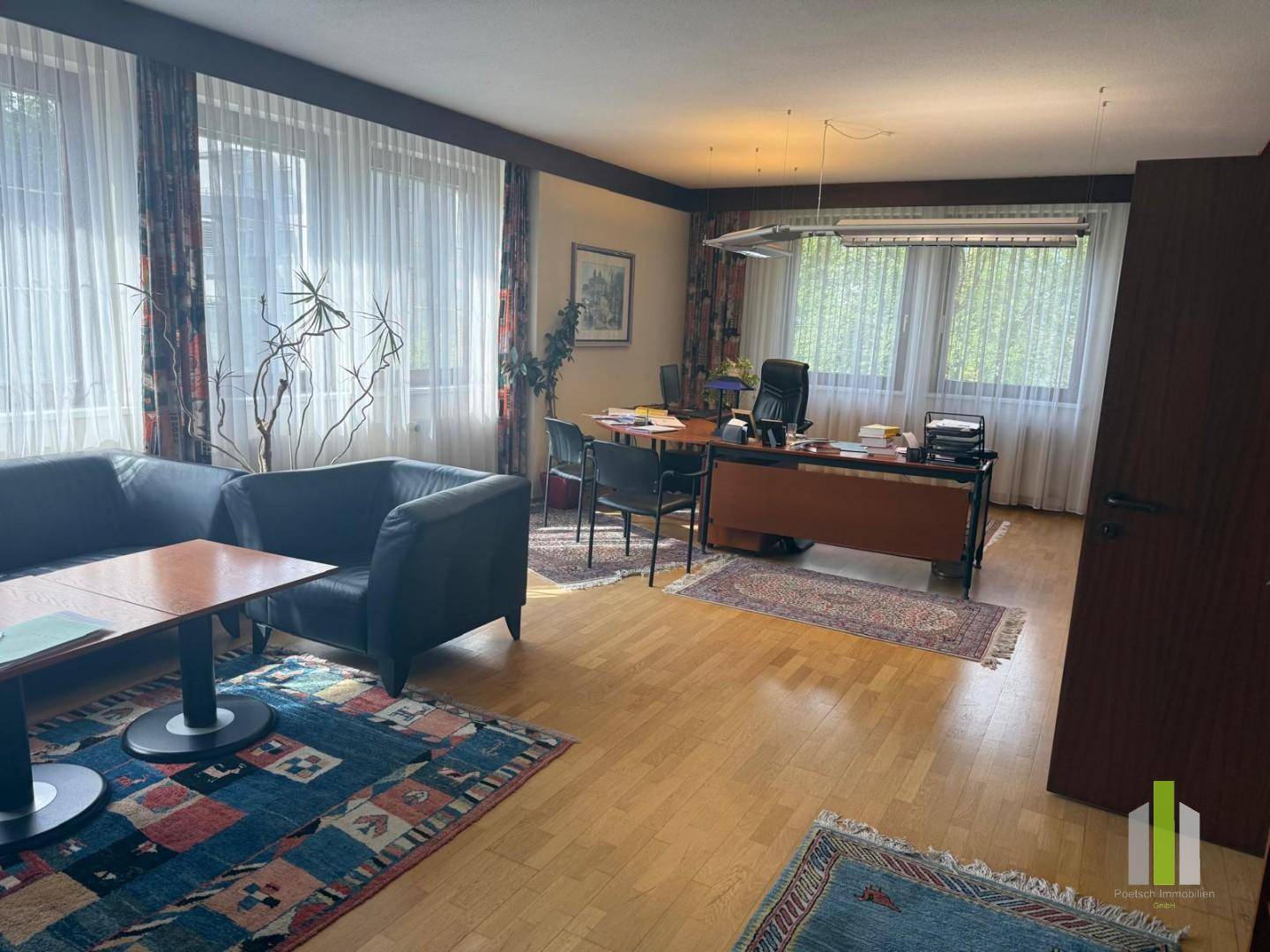 Geräumiges Büro mit Holzboden, großen Fenstern und mehreren Arbeitsbereichen.