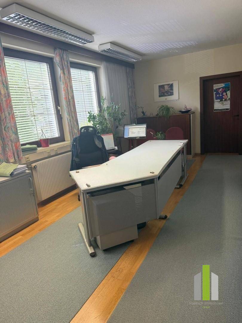 Büro mit Teppichboden, großem Schreibtisch und Heizkörper unter den Fenstern.